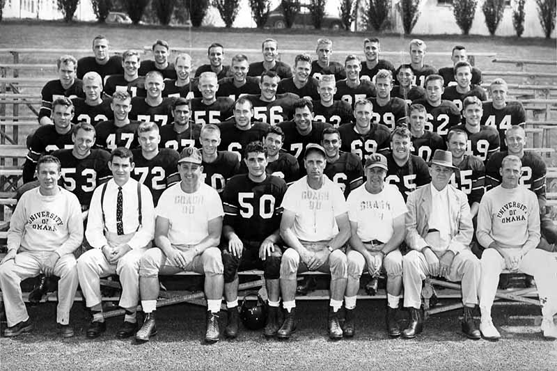 Football players and coaches seated on stadium bleachers for formal team portrait