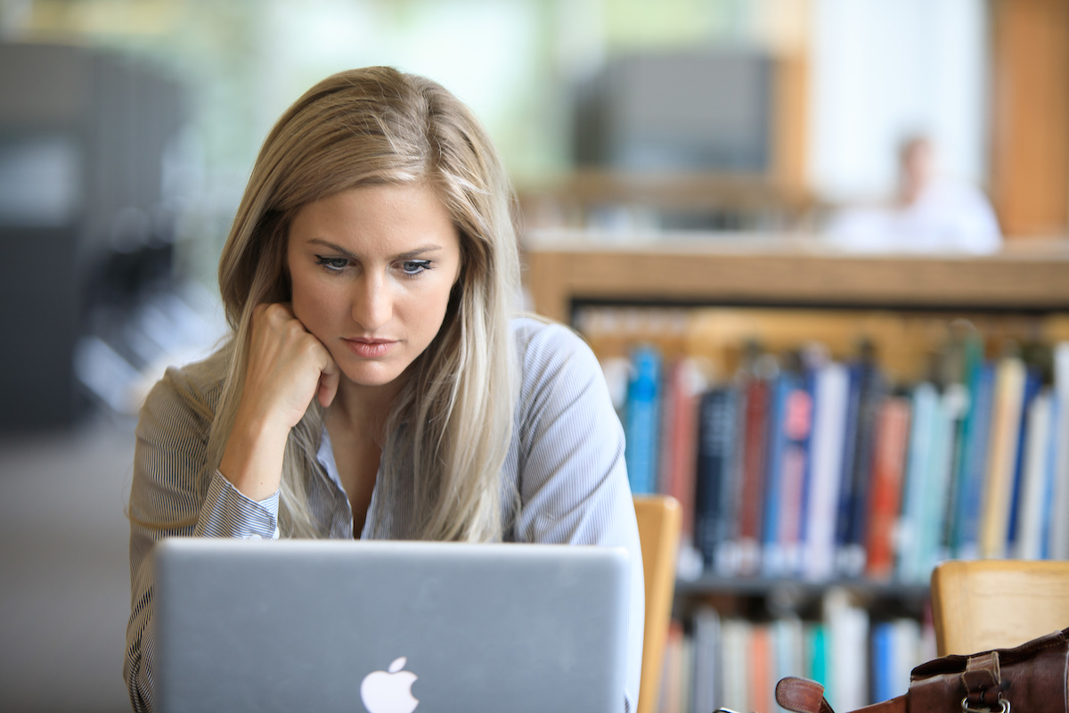 student sitting at table in library on computer, looking intently at the screen.