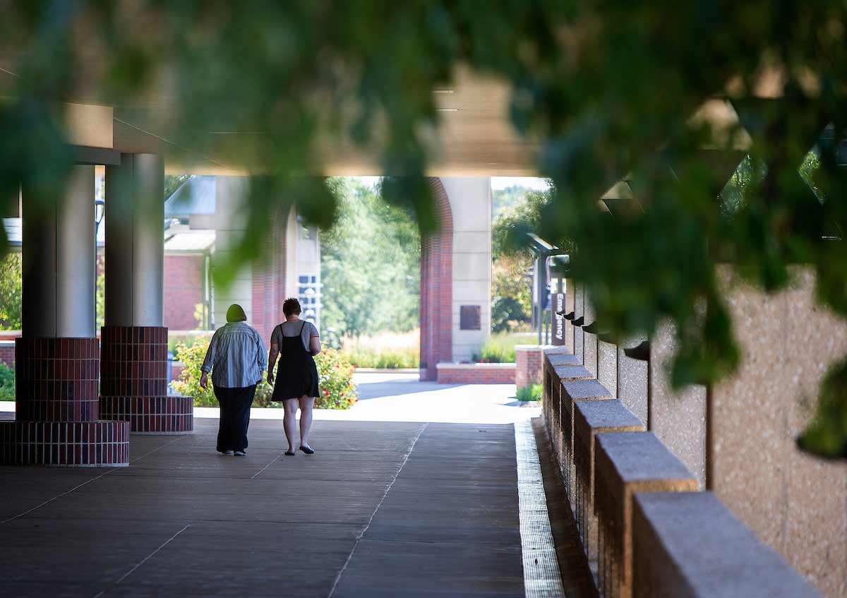 Two staff members walk towards the UNO Henningson Memorial Campanile on the UNO Dodge Campus