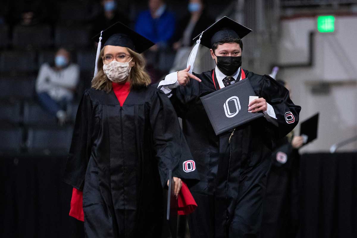 A student points at his degree after crossing the stage.