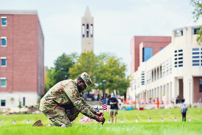 Military service member places small American flags on the UNO campus green.