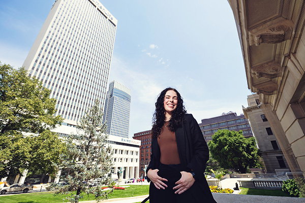 Student sits outdoors on campus with downtown Omaha buildings behind her.