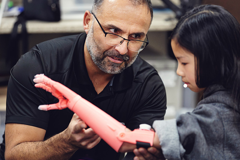 Faculty member helps a young girl test a 3D-printed prosthetic arm.
