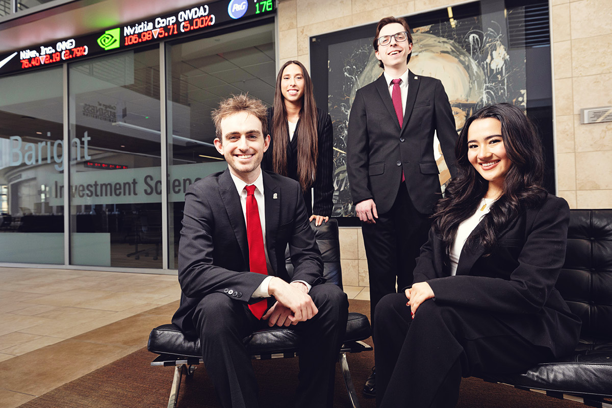Students in business attire pose in front of a financial ticker display.