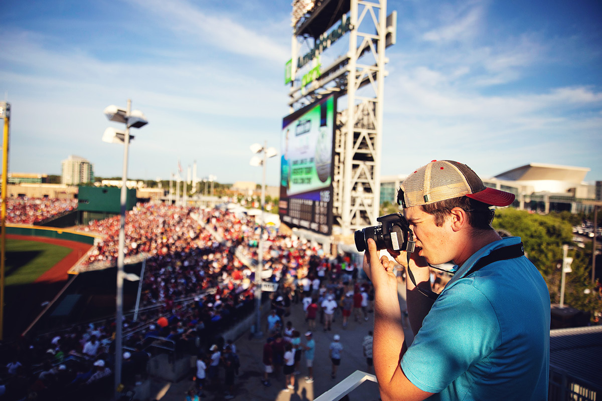 A student films from the stands at a baseball stadium.