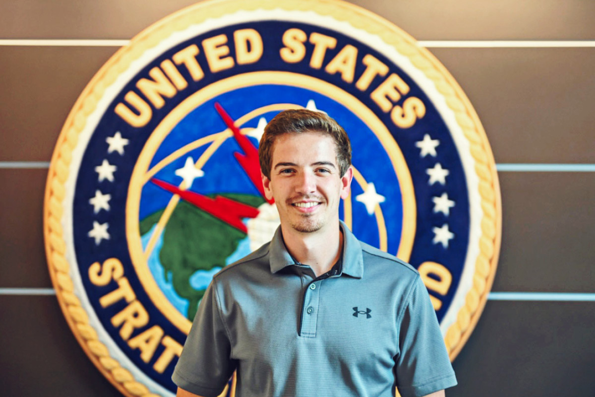 A student stands in front of a large emblem for the United States Strategic Command.