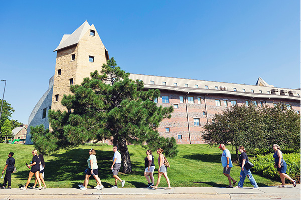 Students walk past a campus building with green lawns.