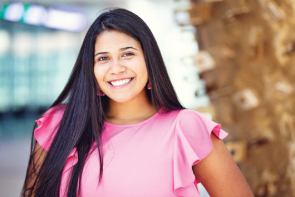 A student stands smiling in front of palm-like campus landscaping.