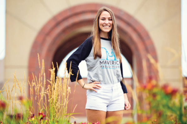 A student stands smiling in front of a campus sculpture.