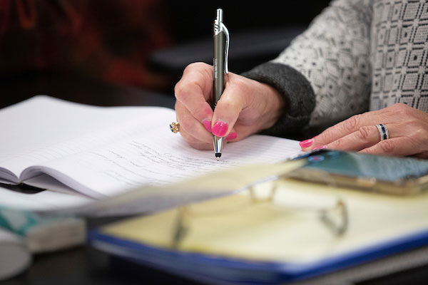 Hand with pen doing some writing on a notepad.