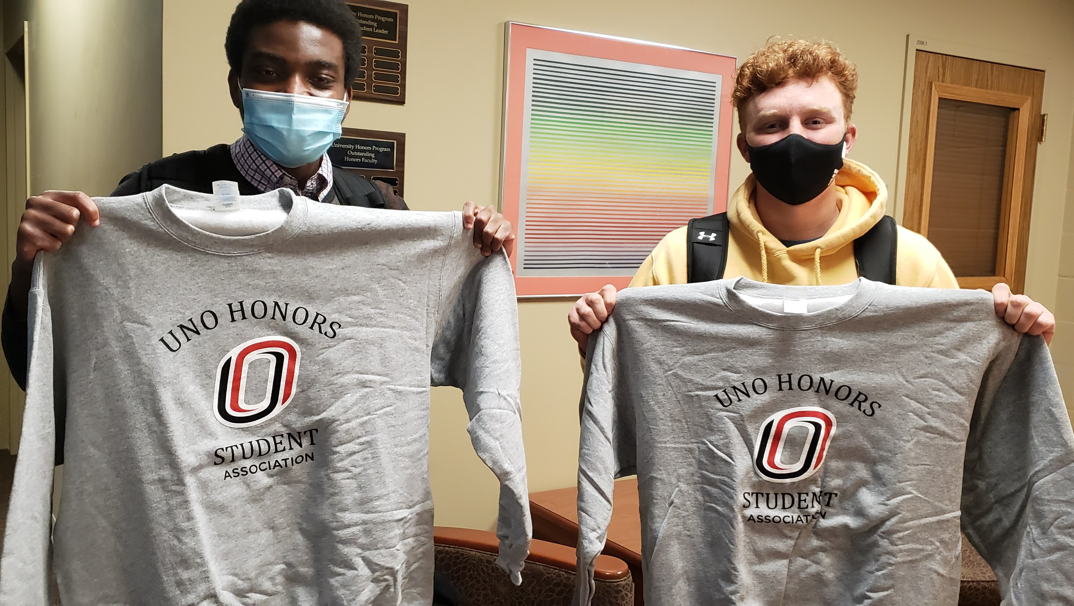 Two students holding up grey UNO Honors Association sweatshirts