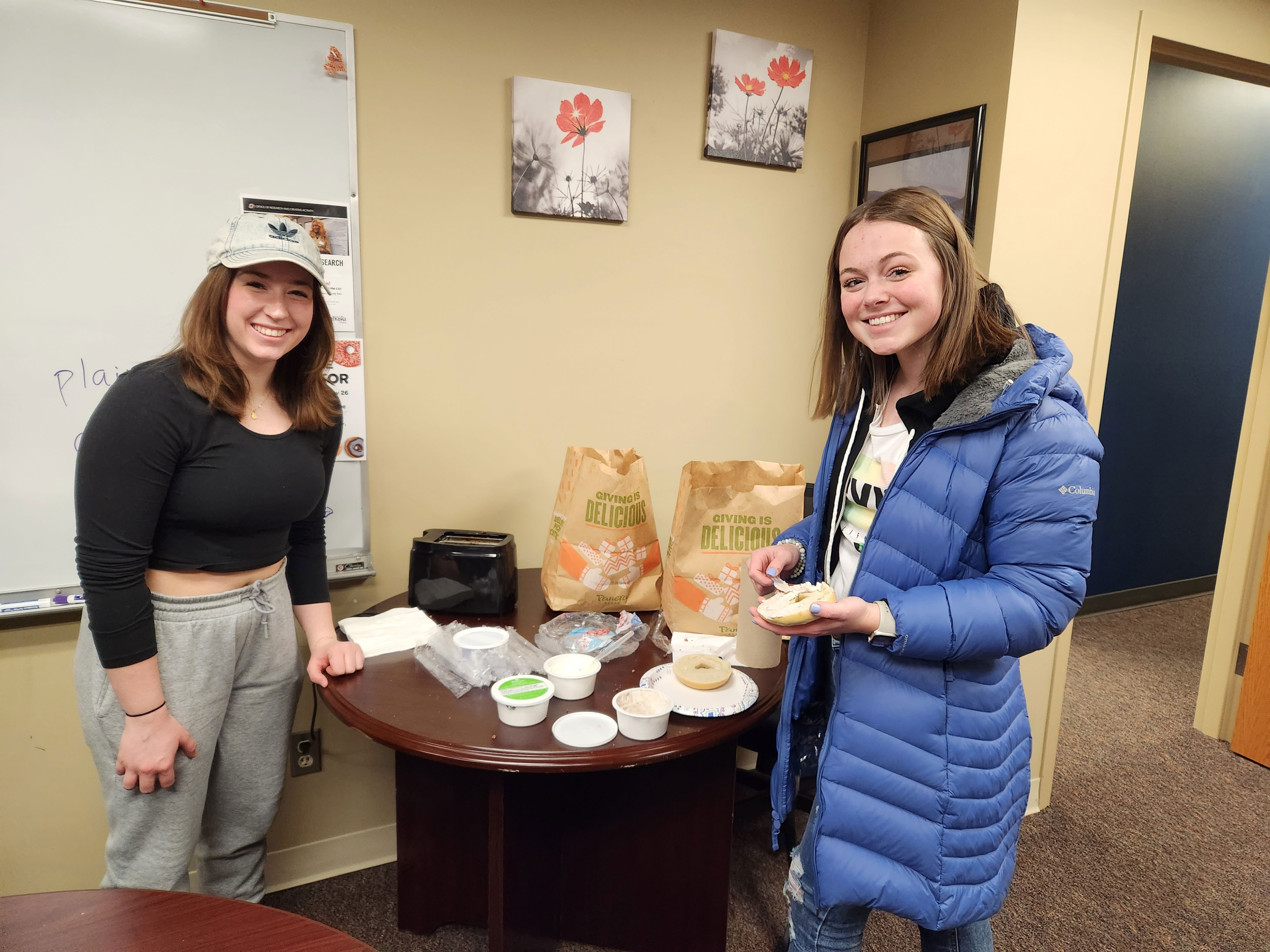 Two smiling Honors students standing at a round table with bagels in their hands