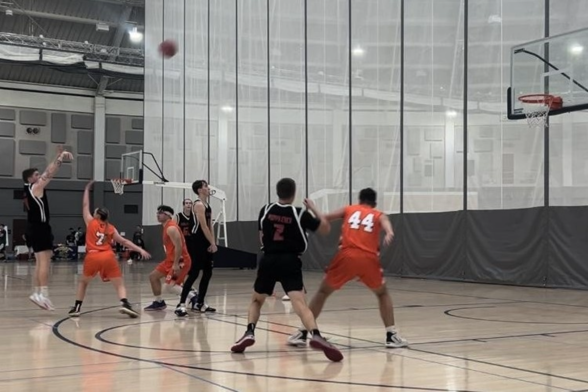 UNO Det 470 basketball game against Syracuse University’s ROTC. A UNO player has thrown the ball toward the basketball hoop. Several other players from both teams watch to see if the ball will go in.