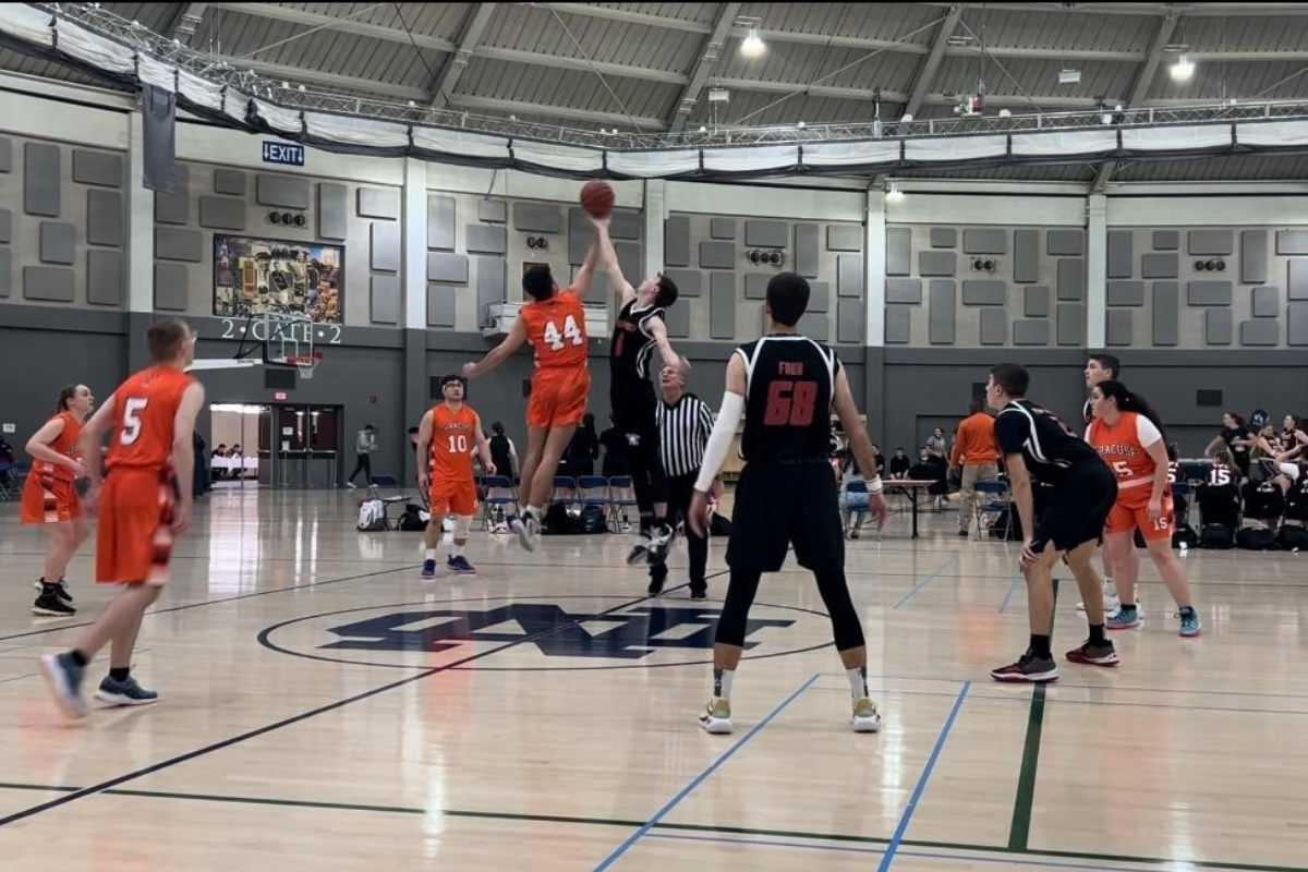 UNO Det 470 Basketball team plays against Syracuse University’s ROTC. A Syracuse player and a UNO player both jump for the basketball with the UNO player getting the ball. Several other players from both teams are standing in a circle around the two players jumping for the ball.