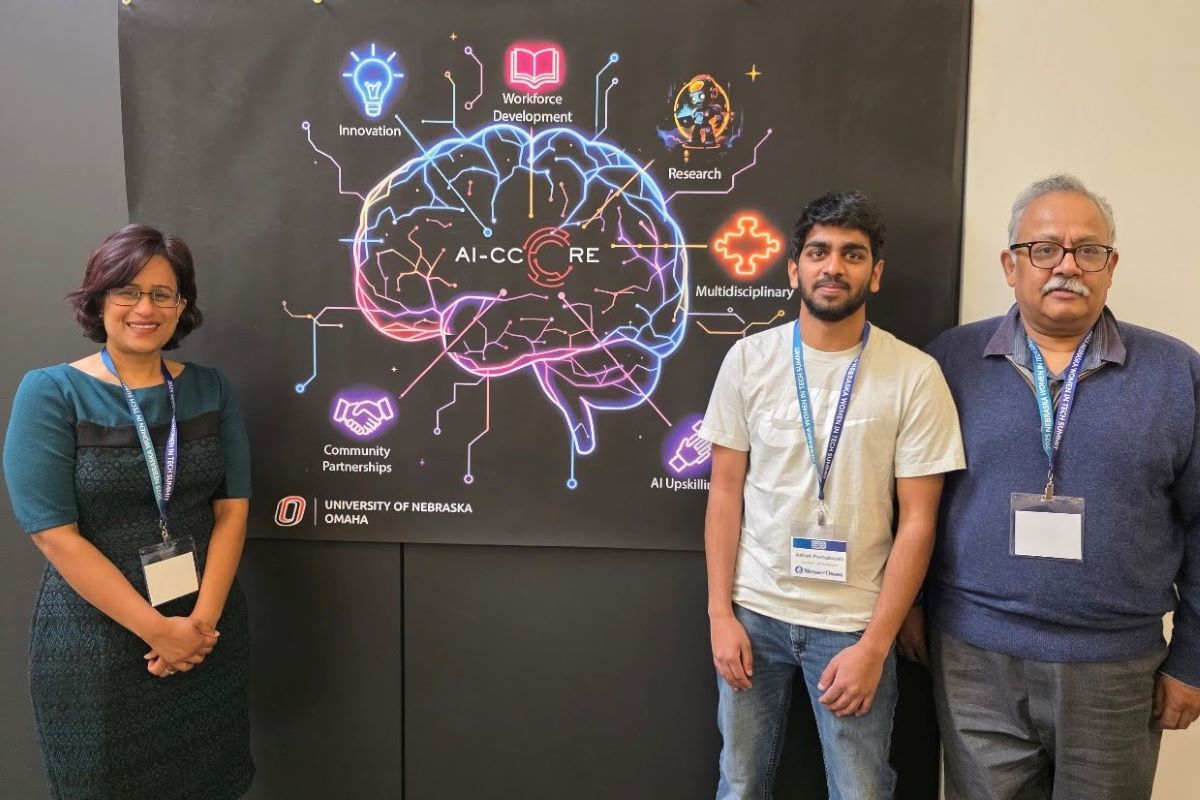 Three people pose in front of the AI-CCORE poster featuring a neon brain graphic highlighting AI-related themes, including research and workforce development.