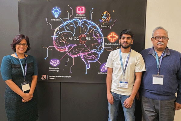 Three people pose in front of the AI-CCORE poster featuring a neon brain graphic highlighting AI-related themes, including research and workforce development.