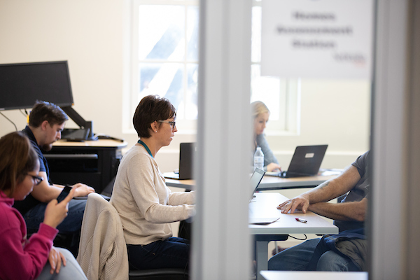 a woman works on a laptop in a room full of people