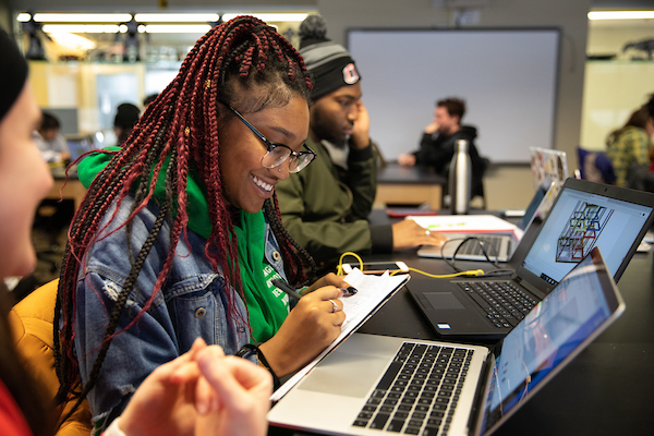 an african american woman smiles as she takes notes in a notebook