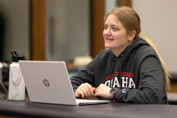 a woman sits at a table with her laptop open in front of her