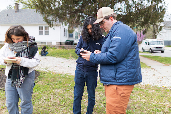 a group of people stand in a neighborhood looking at information