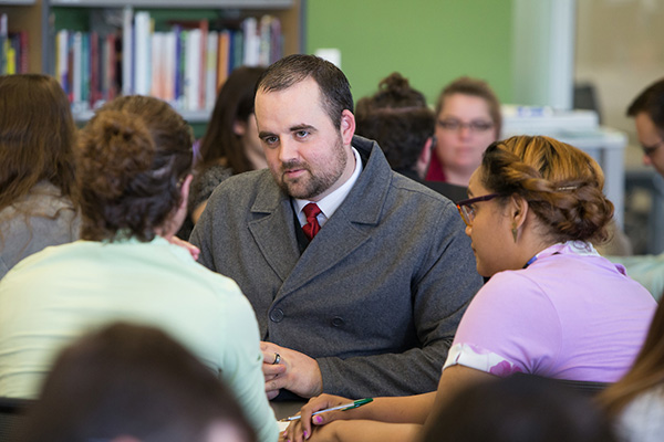 a man sits at a table and speaks to a group of students