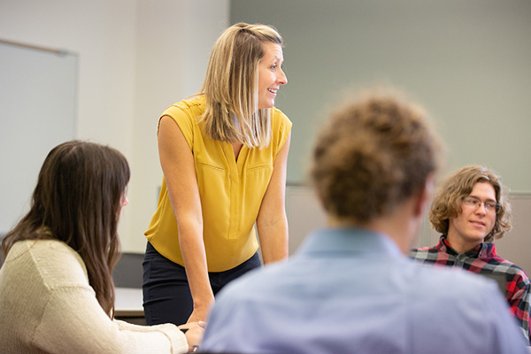 a woman leans on a desk as she talks to students