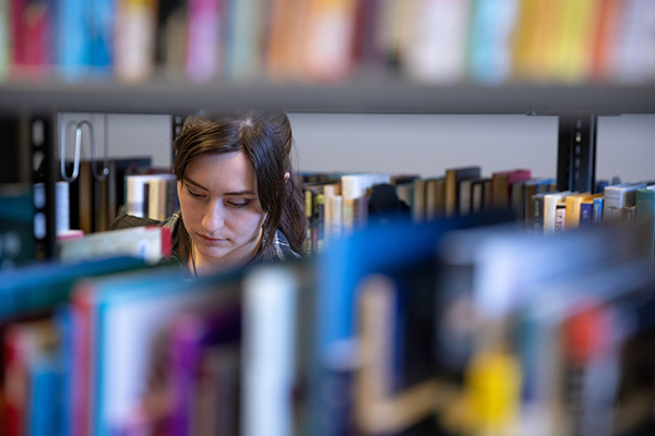 a woman stands among the bookcases in a library