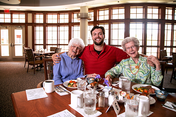 a man sits between two well-dressed elderly women