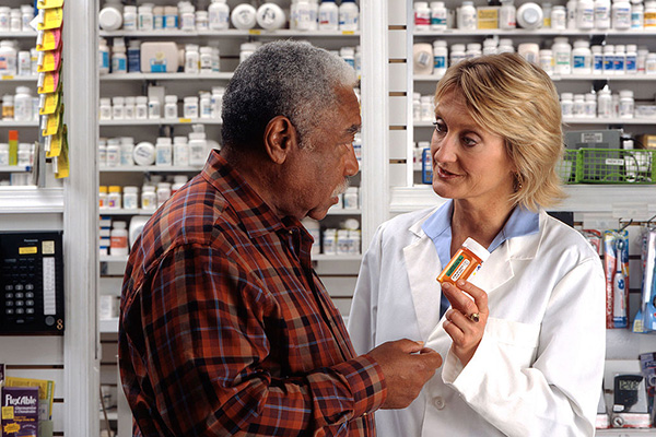 An older African-American man talks to a white female pharmacist as she explains his prescription.