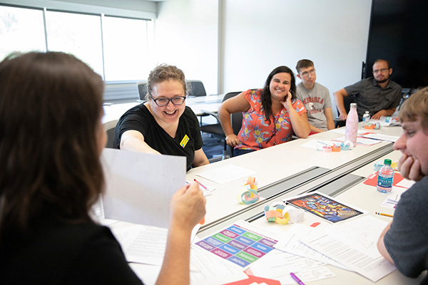 a group of people sits around a table creating art and smiling