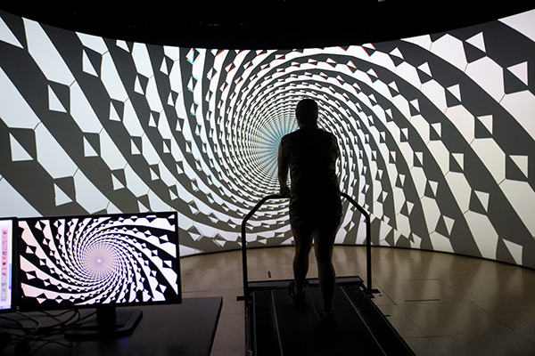 a person walks on a treadmill in front of a black and white spiral screen