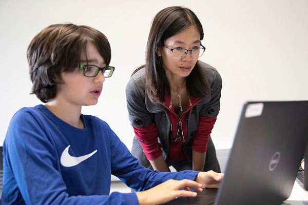 a female teacher looks at the laptop sscreen of a young student