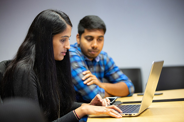 a woman and man sit at a table working on a laptop