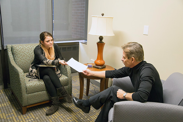 a woman is sitting in a chair hands a piece of paper to a man i a chair across from her