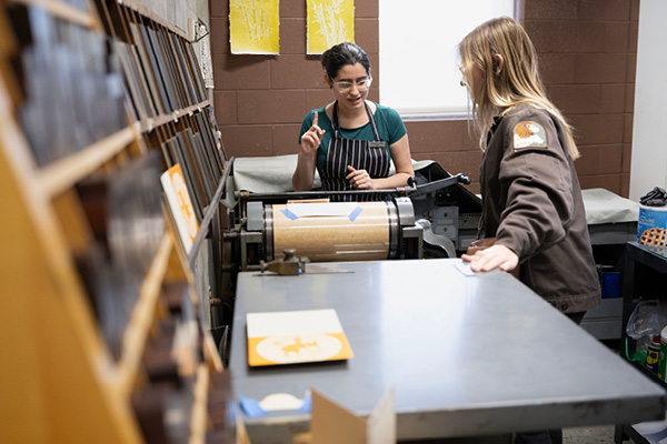 A teacher showing a student how to use the printing press to make cards.