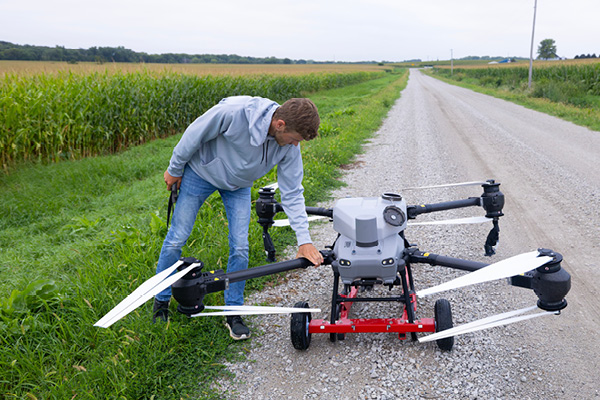 A male student in a field adjusting the wings of a drone.