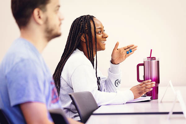 student raises her hand while speaking with classmates.