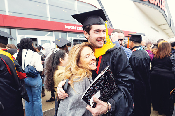 A graduate in cap and gown hugs a supporter outside Baxter Arena after the commencement ceremony.