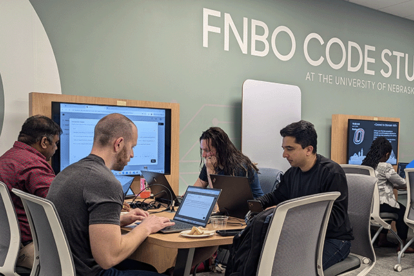 students sit together at a table looking at a screen.