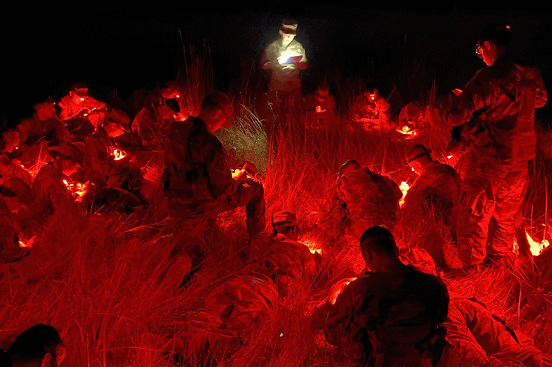 young soldiers in a field at night that is glowing red from their lights.