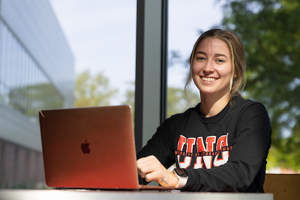 a young woman with blond hair sits at a table with her laptop in the wellness center.
