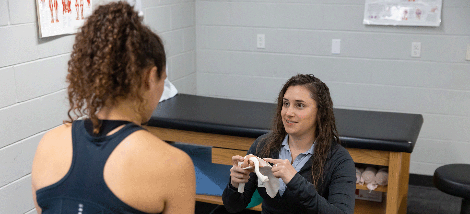a young woman sits on an exam table and talks to a provider.