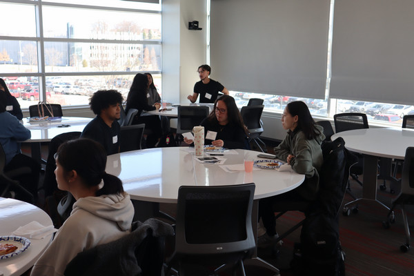 group of students discussing about an image while seating around a round white table in a classroom.