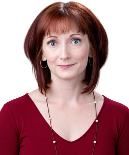Portrait of a person with short auburn hair and bangs, wearing silver hoop earrings, a burgundy V-neck top, and a long beaded necklace, looking at the camera with a slight smile against a transparent background.