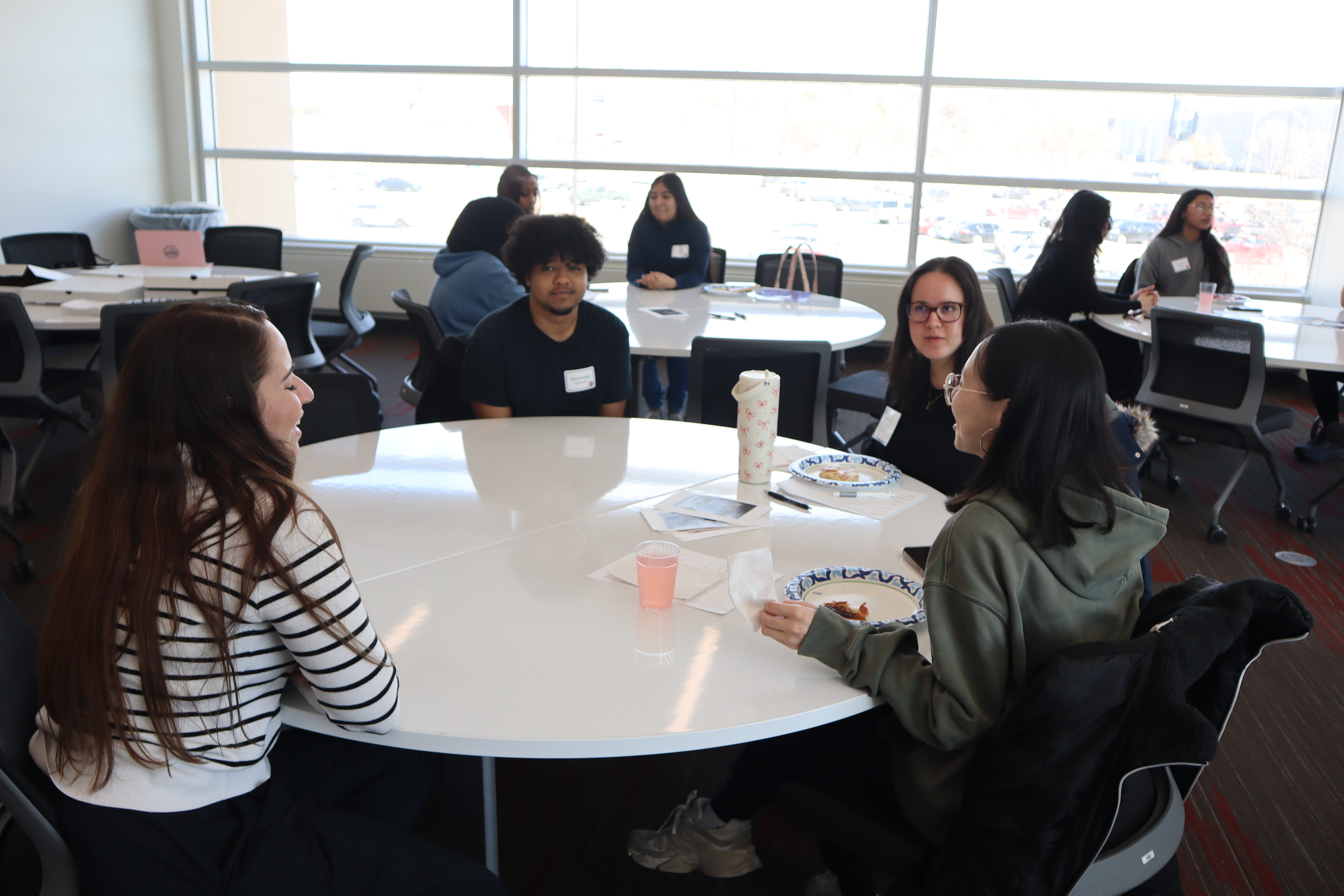 UNO students in a round gray table in a classroom, talking to each other, discussing a project.