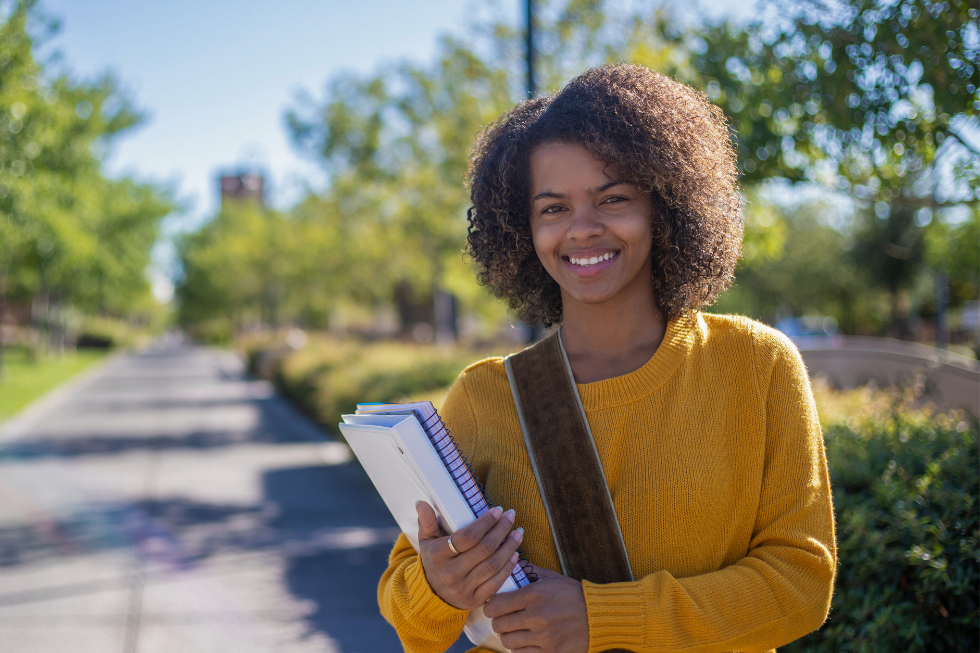 A student smiles while holding textbooks.