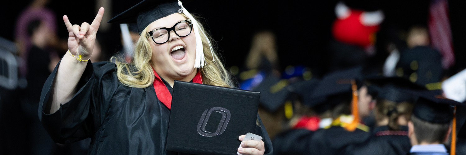 A graduate holds their diploma and smiles. 