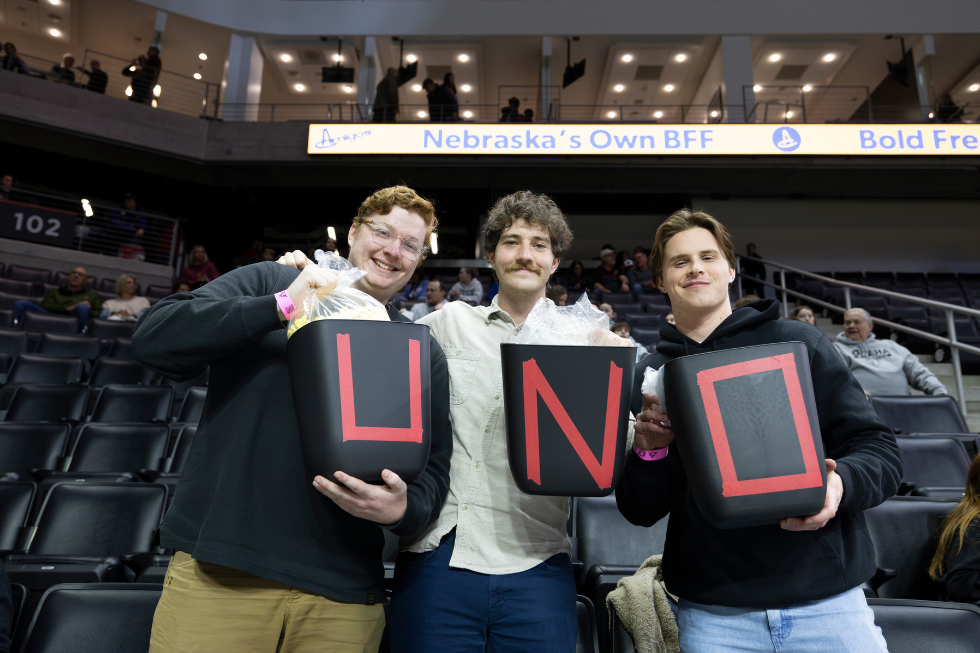 three students holding U N O trash bins for a volunteer event at Baxter Arena