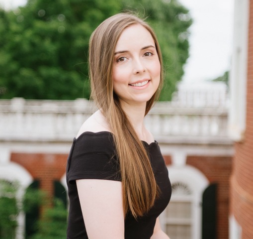 Dr. Olivia Christley looking over her right shoulder wearing a black top in front of a red brick building with white windows