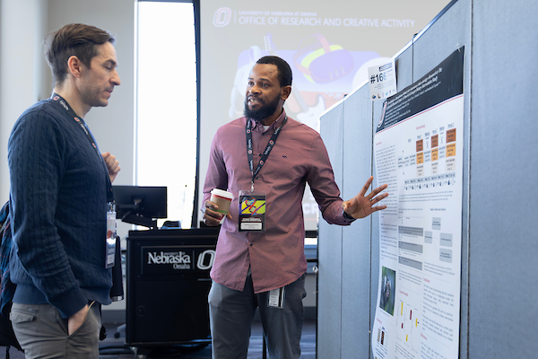 a black man discusses his research poster with an older white man.